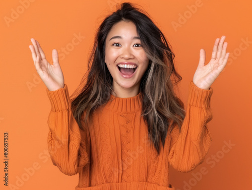 A woman in an orange sweater is smiling and raising her hands in the air photo