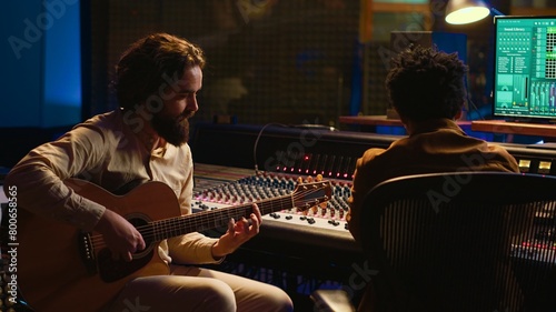 Obraz na plátně Creative artist singing on his electro acoustic guitar to record new track, producing music in control room at professional studio