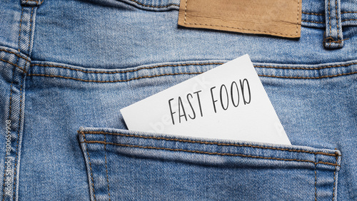  White card with a handwritten inscription "Fast Food", inserted into the pocket of blue pants jeasnow (selective focus)