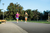 Two active young latin women jogging vigorously in a green urban park in a sunny afternoon. Running session.