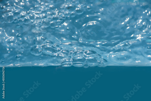 Bluewater waves on the surface ripples blurred. Defocus blurred transparent blue colored clear calm water surface texture with splash and bubbles. Water waves with shining pattern texture background.