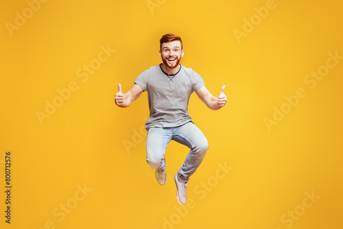 Happy joyful man jumping up in air, demonstrating thumbs up