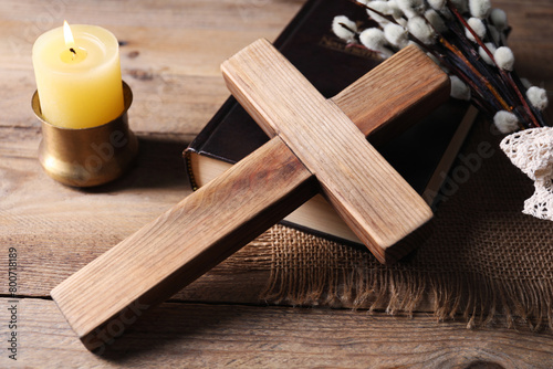 Cross, Bible, burning church candle and willow branches on wooden table, closeup