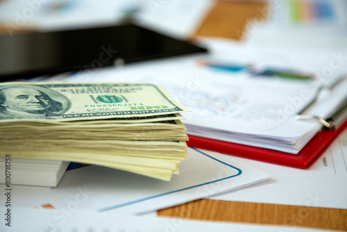 Symbolizing corporate earnings and economic analysis, stack of US dollars rests on business desk alongside financial charts and graphs, illustrating financial insights