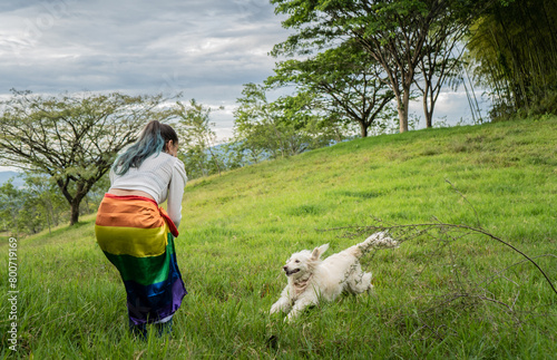 mujer joven al aire libre usando la bendera gay en su cintura y jugando con su perro  photo