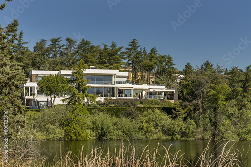 a beautiful modern style mansion house surrounded by trees on the shore of a lake