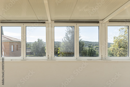 Front image of a wall with aluminum and glass windows with good views of the mountain with trees on a bright day