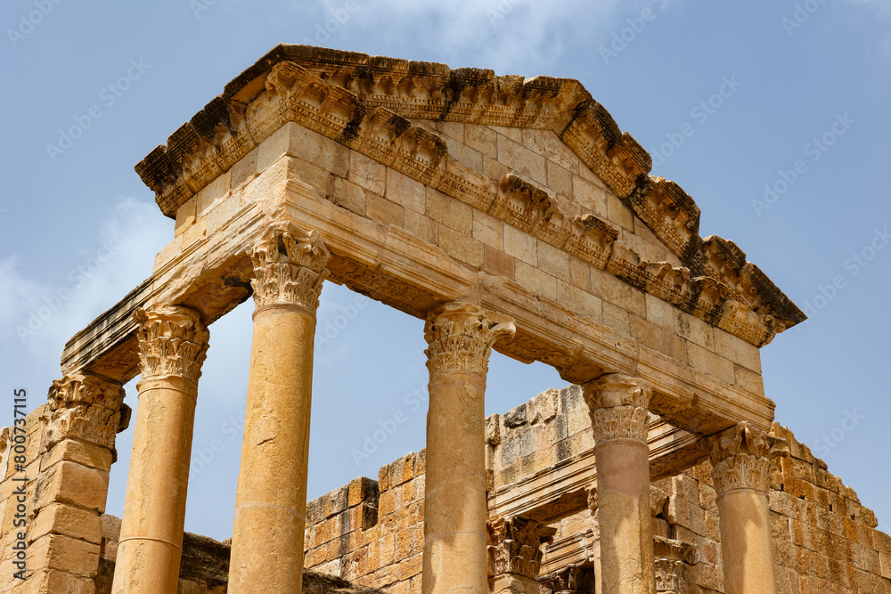 Detailed view of remnants of Capitoline Temple at Tunisian archaeological site of Sbeitla with weathered carved Corinthian columns supporting pediment against blue sky