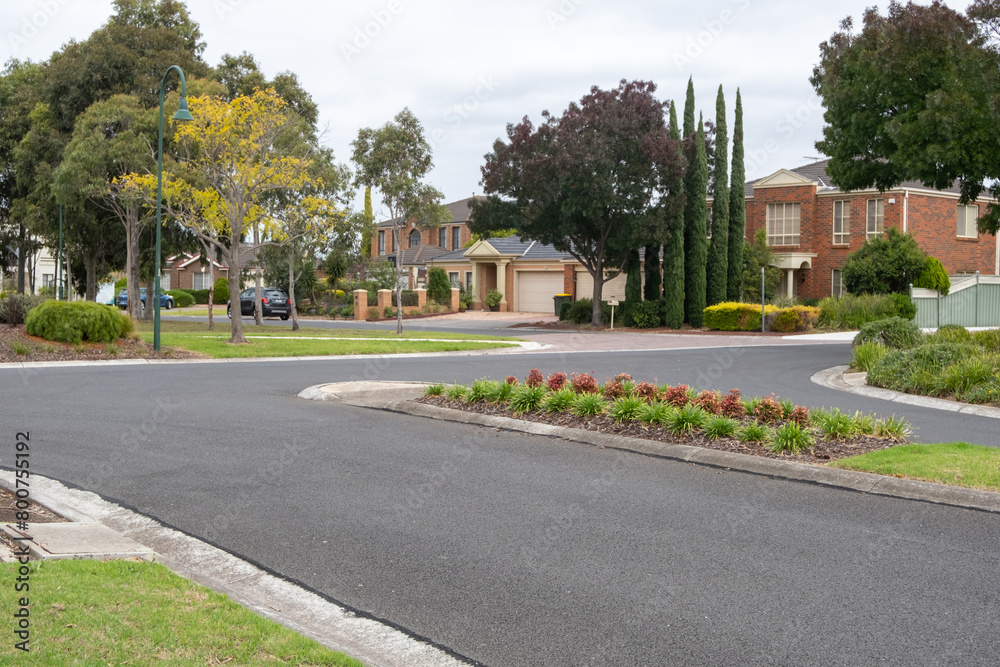 A suburban road with a T-intersection and a median nature stripe in the middle, with residential suburban houses in the distance. It's a quiet, clean, and beautiful neighborhood street in Australia.