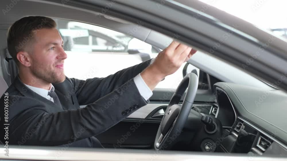 A young buyer in a business style sits in the interior of a new car and looks at it A young buyer in a business style sits in the interior of a new car and looks at it