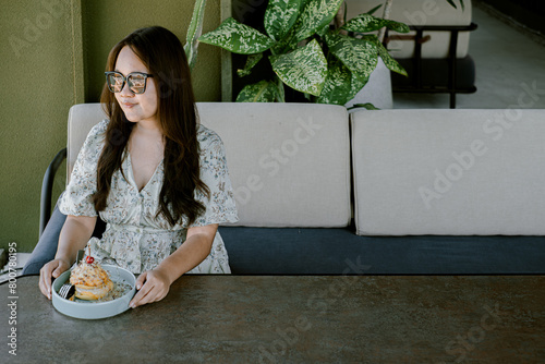 An Asian woman sits and eats a cake in the semi-outdoor dining area. The woman was wearing a tropical dress and sunglasses. © David