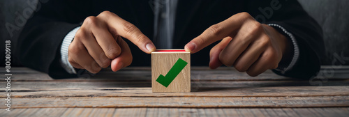 A person's fingers hold a wooden block displaying a green checkmark, symbolizing confirmation photo