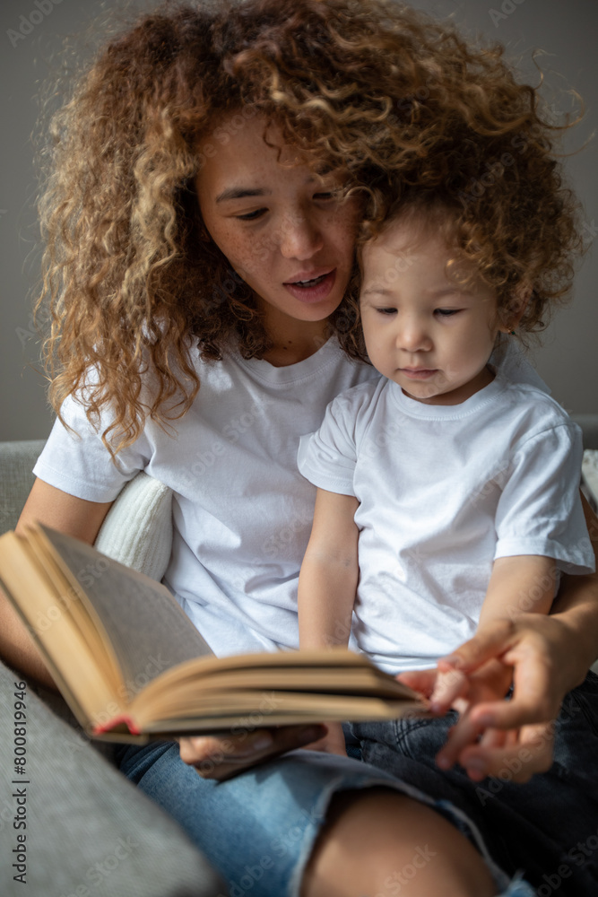 Curly mother and daughter in white T-shirts reading a book Curly mother and daughter in white T-shirts reading a book