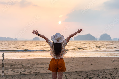 Happy woman traveler, arms rised, enjoying sunset at sea, Phuket and Krabi travel sounthern Thailand.