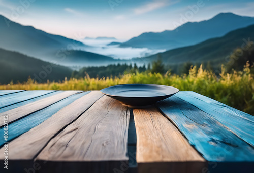 A black plate on a rustic blue wooden table overlooking a scenic mountain landscape with morning mist.