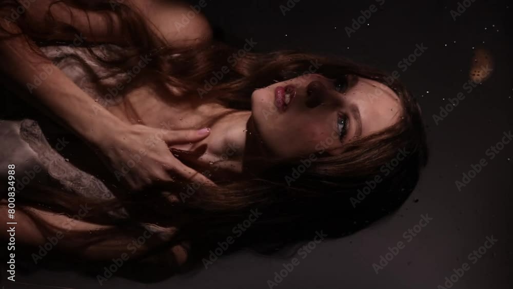 A woman behind glass with water flowing down it. The water reflects her face, creating a distorted and dreamy effect. Woman is holding a leafy green plant in her hand. A woman behind glass with water flowing down it. The water reflects her face, creating a distorted and dreamy effect. Woman is holding a leafy green plant in her hand.