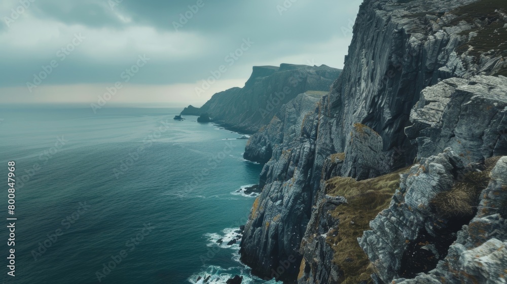 A rocky cliff juts out over the turbulent ocean below, with crashing waves against the base. The sky is filled with dark clouds, hinting at an impending storm.