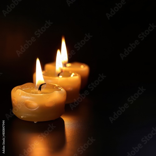 Three flickering candles illuminate the darkness  casting a warm glow against the black background  creating a serene and enchanting ambiance