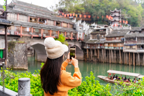 Young female tourist taking a photo of the Feng Huang Ancient Town, The famous tourist destination at Hunan Province, China © Kittiphan