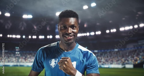 Soccer Player Presentation: Handsome Black Footballer Posing, Looking at Camera and Smiling. Confident Young Man in Blue Uniform Holding a Ball and Getting Pumped Up Before a Tournament Match photo