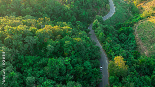 Aerial view of dark green forest road and white electric car Natural landscape and elevated roads Adventure travel and transportation and environmental protection concept 