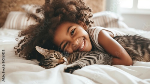 A little girl tenderly hugs her kitten and lies on the bed in the morning in a bright bedroom. Friendship concept between child and pet, copy space for text 