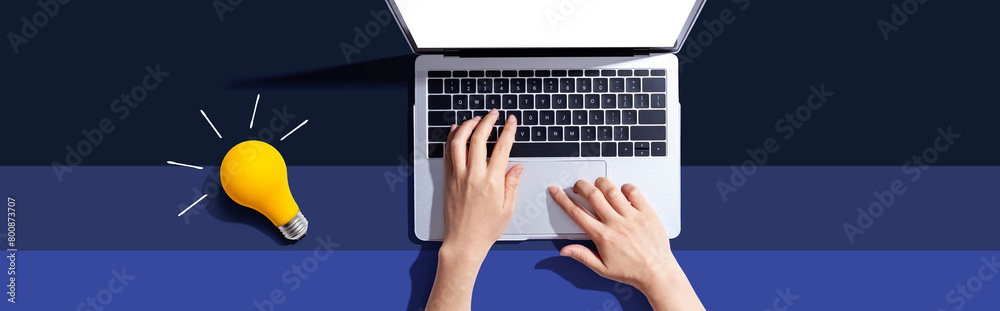 Person using a laptop computer and a light bulb - Flat lay Person using a laptop computer and a light bulb - Flat lay