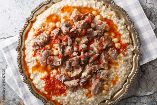 Traditional Turkish Wheat Stew With Mutton Meat, with butter and red pepper sauce closeup on the plate on the table. Horizontal top view from above © FomaA