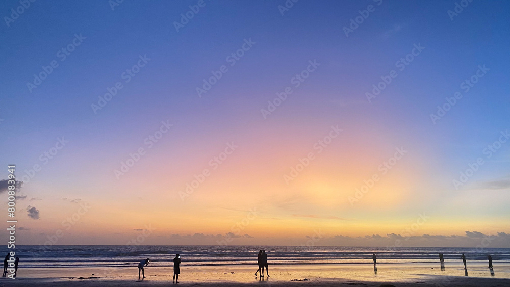 beautiful orange sunset with people on the beach and a pink, purple and blue sky.