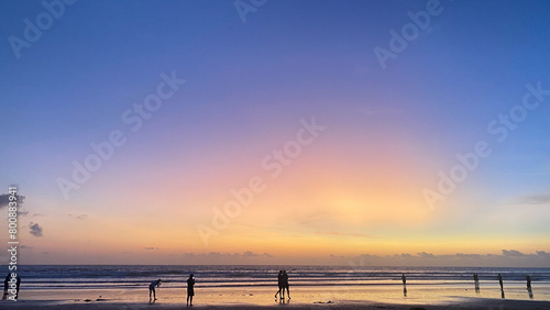 beautiful orange sunset with people on the beach and a pink  purple and blue sky.
