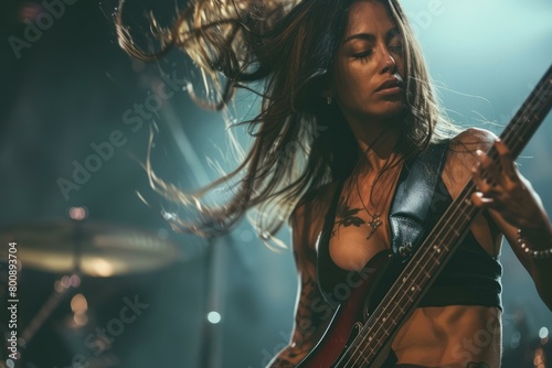 Portrait of a female musician playing the bass guitar on stage with long brown hair and wearing a black leather vest photo
