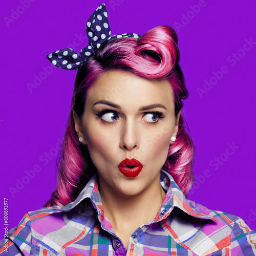 Wow! Excited surprised woman. Pinup girl looking sideways. Purple head model at retro fashion and vintage concept. Isolated against bright color background. Square image. © vgstudio