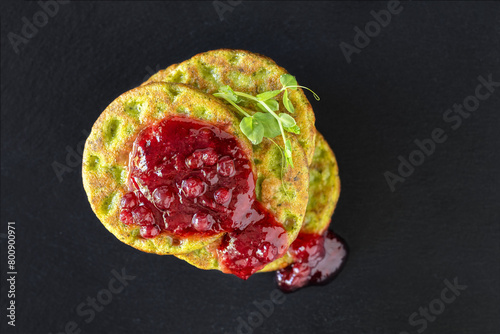 Spinach pancakes with berry jam on the black background, view from top