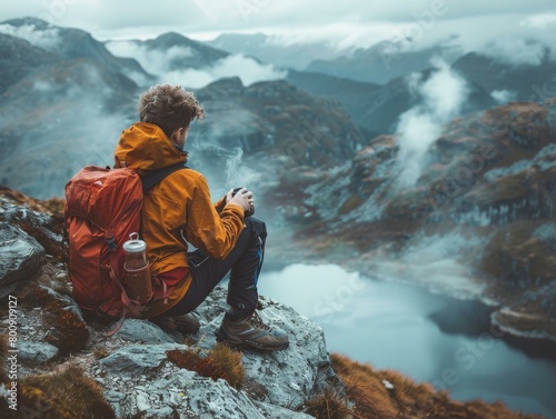 Man in orange jacket sits on rock overlooking mountain valley