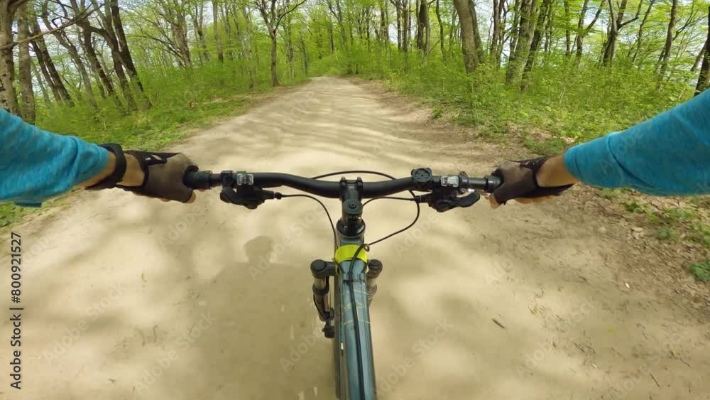 A first-person cyclist riding on a dirt road amidst the forest. Movement and speed create a sense of thrill and adventure. A man on a mountain bike riding down a mountain A first-person cyclist riding on a dirt road amidst the forest. Movement and speed create a sense of thrill and adventure. A man on a mountain bike riding down a mountain