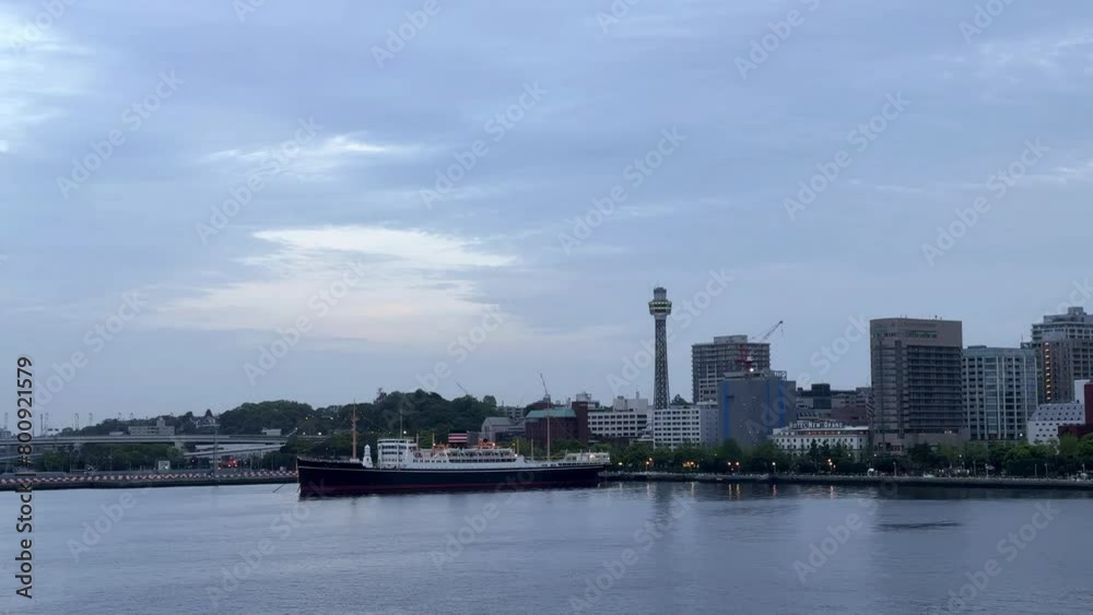 Dusk settles over city skyline with iconic tower and moored ship, gentle water in the foreground Dusk settles over city skyline with iconic tower and moored ship, gentle water in the foreground