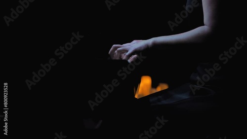 Pianist immersed in playing a black grand piano. The pose of the musician speaks of professionalism and dedication. Solo performance of a female pianist on a dark stage photo