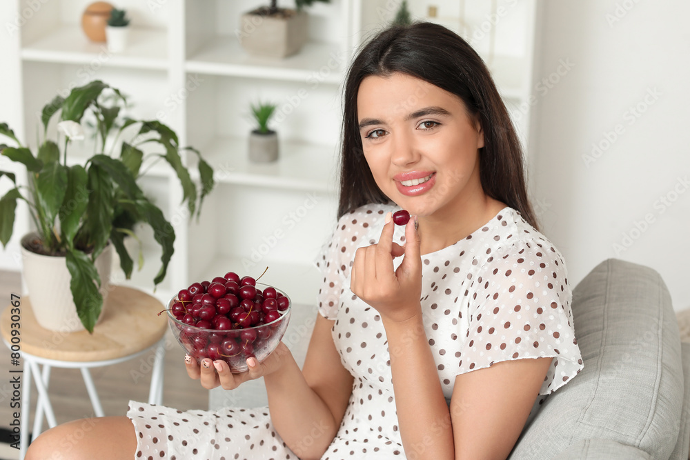 Happy beautiful young woman with bowl of ripe cherries sitting on sofa in living room Happy beautiful young woman with bowl of ripe cherries sitting on sofa in living room