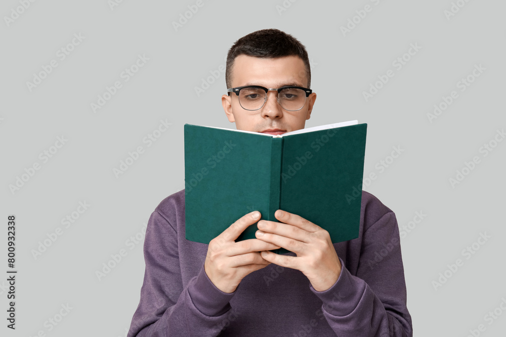 Handsome young man reading book on grey background Handsome young man reading book on grey background