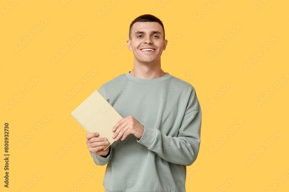 Handsome young man with book on yellow background Handsome young man with book on yellow background