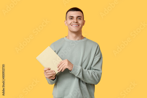Handsome young man with book on yellow background