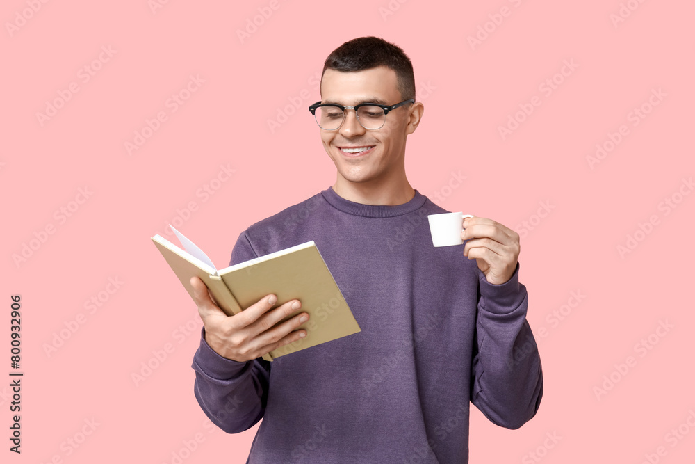 Handsome young man reading book and drinking coffee on pink background Handsome young man reading book and drinking coffee on pink background