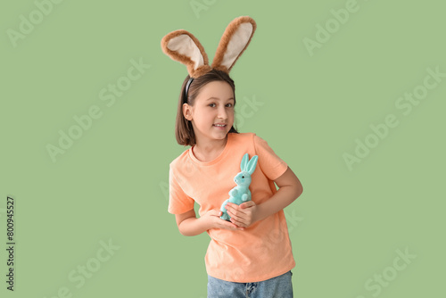Happy little girl in Easter bunny ears with toy rabbit on green background