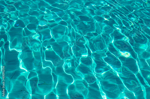 Waves on the light of the pool water. Swimming pool with blue water. Water surface texture. View from above.