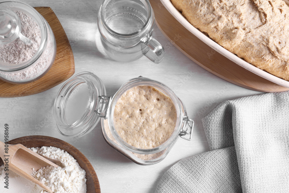 Sourdough starter in glass jar, flour, dough and water on light table, flat lay Sourdough starter in glass jar, flour, dough and water on light table, flat lay