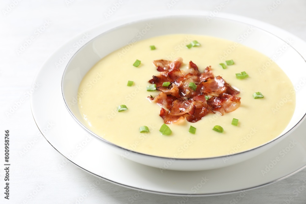 Tasty potato soup with bacon and green onion in bowl on white table, closeup