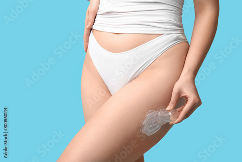Beautiful young woman with vacuum jar and anti-cellulite cream on blue background, closeup