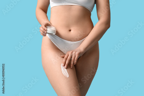 Beautiful young woman with jar of anti-cellulite cream on blue background, closeup