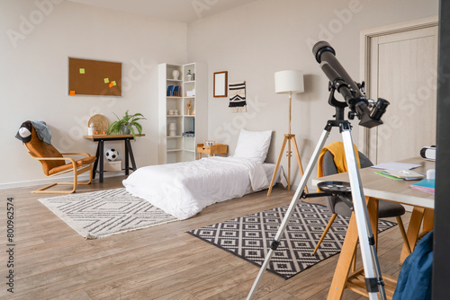 Interior of student's bedroom with bed, armchair and telescope