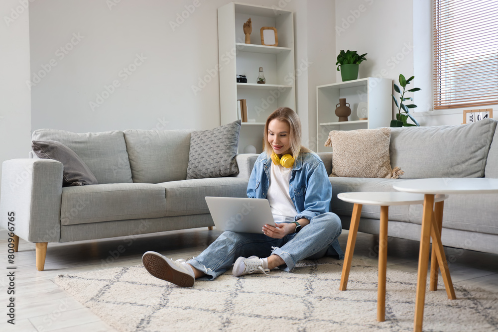 Young woman in headphones using laptop on floor in light living room Young woman in headphones using laptop on floor in light living room